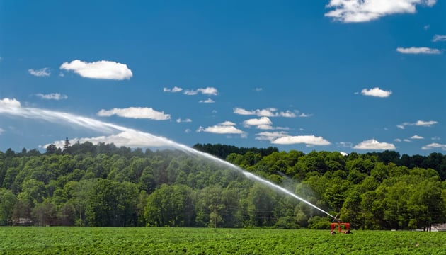 Agricultural irrigation system watering a green crop field under a blue sky, representing smart farming and IoT solutions for precision agriculture and water management.