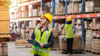 Warehouse workers wearing safety vests and hard hats inspecting inventory, representing IoT asset tracking and warehouse management solutions.