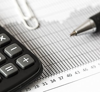 Close-up of a calculator, pen, and financial chart on paper, representing tax reporting, financial analysis, and business accounting processes.