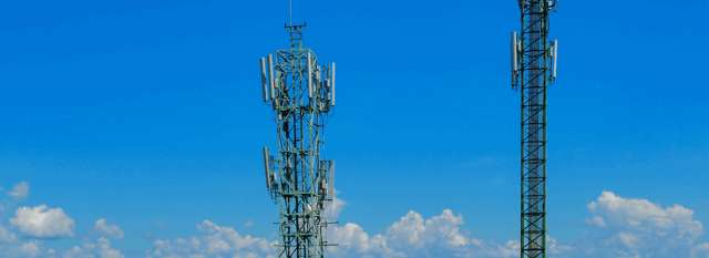 Two cellular network towers against a bright blue sky, representing 4G vs 5G connectivity and advancements in IoT communication technology.