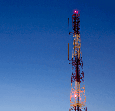 Cellular communication tower with antennas and red signal lights against a blue evening sky, representing IoT connectivity and 4G LTE network infrastructure.