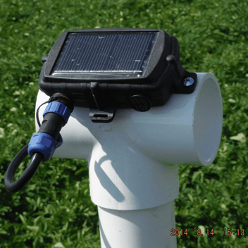 Solar-powered GPS tracking device mounted on a white PVC pipe in a green field, representing sustainable IoT asset tracking and remote monitoring solutions.