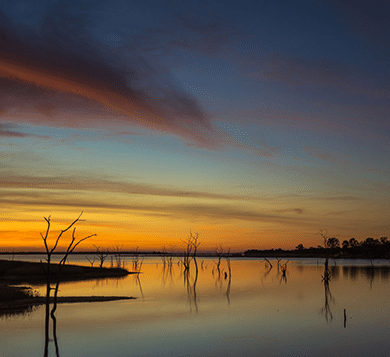 Beautiful sunset over Lake Kariba with calm waters and silhouetted trees, representing natural tranquility and environmental monitoring potential for IoT applications.