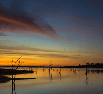 Beautiful sunset over Lake Kariba with calm waters and silhouetted trees, representing natural tranquility and environmental monitoring potential for IoT applications.